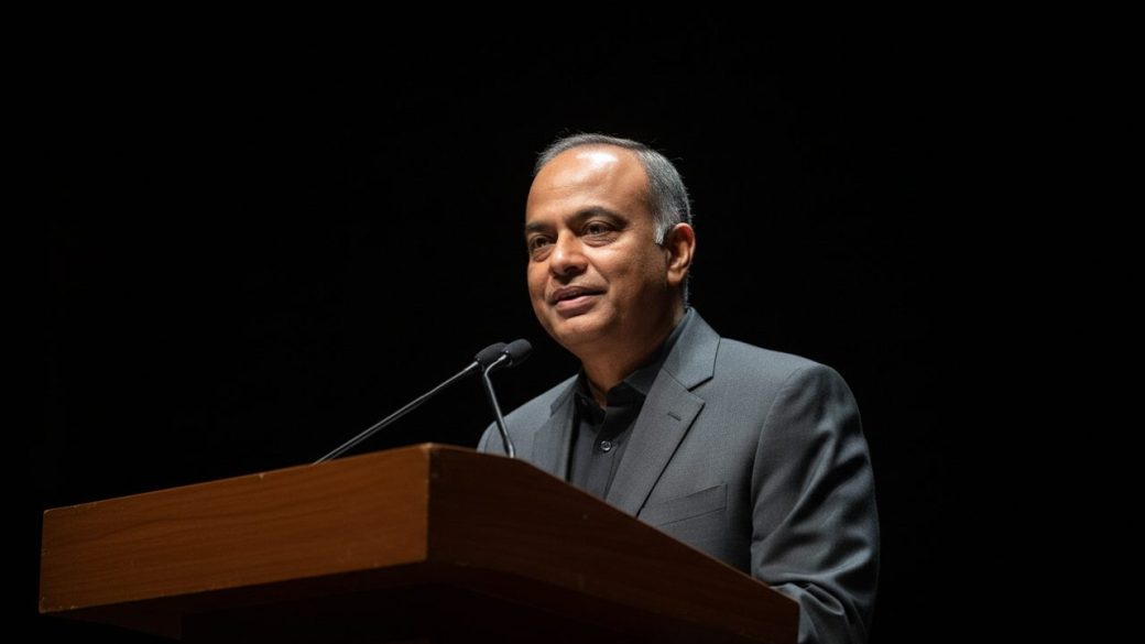 Nandan Nilekani speaking at a podium, calm and confident expression, single spotlight, clean dark background, high contrast, photorealistic portrait