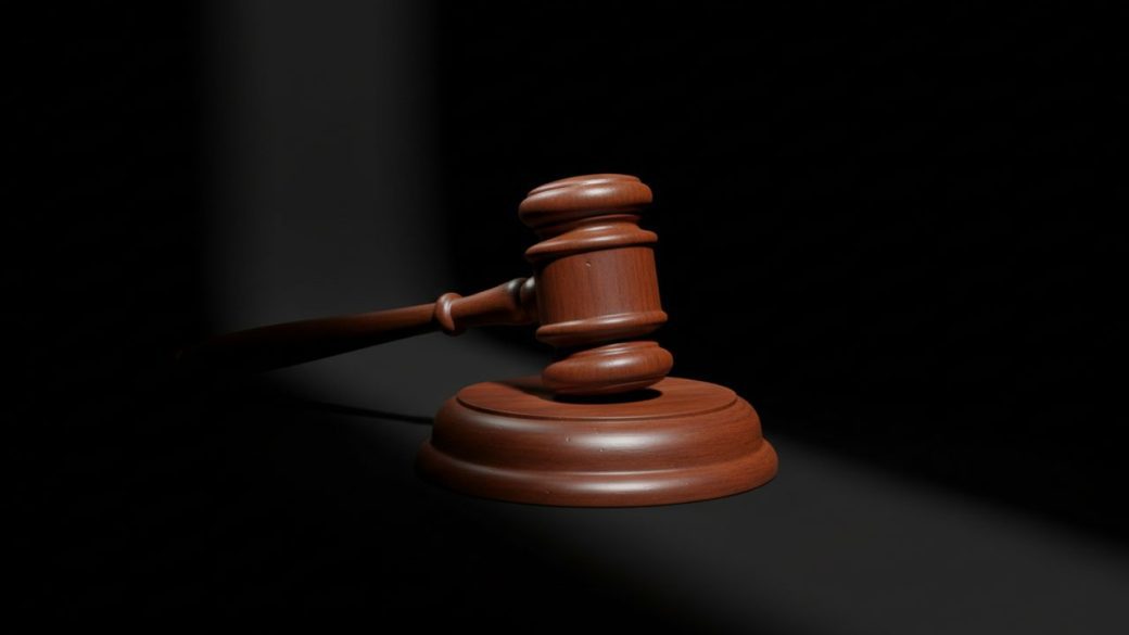 A polished wooden judge's gavel resting on its sound block, lit by a single dramatic beam of light against a clean dark background, high contrast, photorealistic, no text