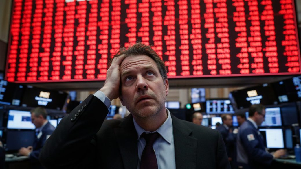 A worried trader on a stock-exchange floor watching a giant red board of falling share prices, deep red downward arrows glowing across the screens