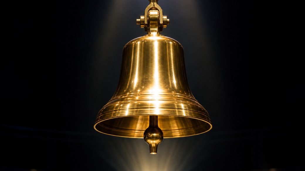 Glowing brass stock-listing ceremony bell on a dark exchange stage, symbolising India's 2026 startup IPO wave