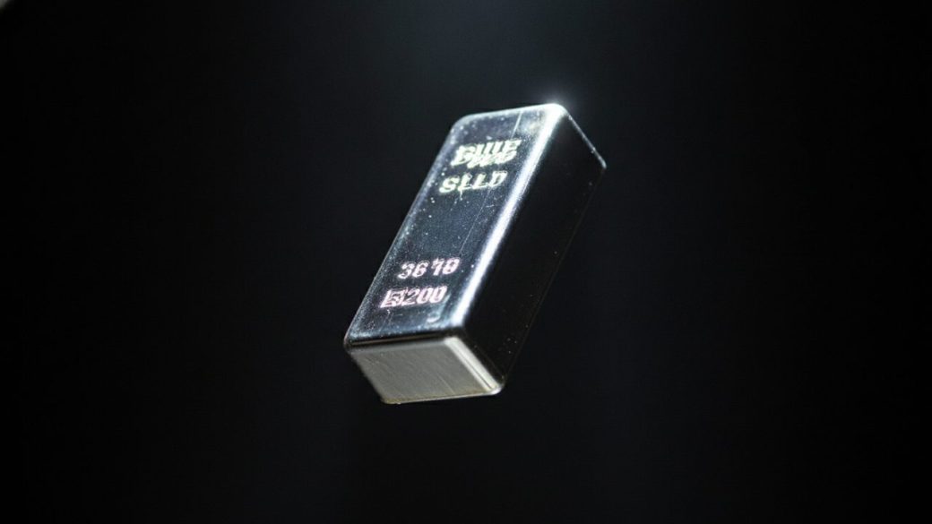 A single gleaming silver bar tumbling against a dark background under sharp high-contrast light, one focal subject, no text or logos